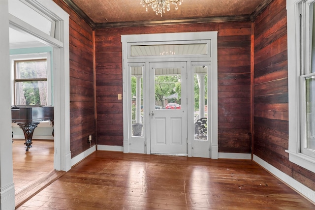 entrance foyer with wood walls, a chandelier, hardwood / wood-style flooring, and crown molding