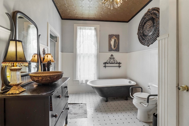 bathroom featuring tile flooring, ornamental molding, a tub, vanity, and toilet