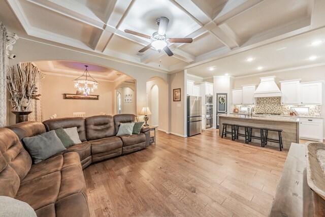 living room featuring ceiling fan with notable chandelier, light hardwood / wood-style flooring, coffered ceiling, and crown molding