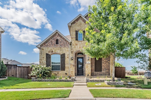 view of front of property with stone siding, brick siding, a front lawn, and fence