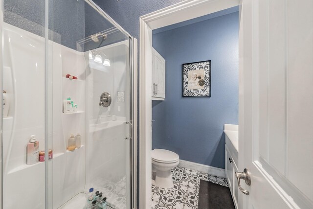 bathroom featuring tile patterned floors, vanity, toilet, and a shower with door