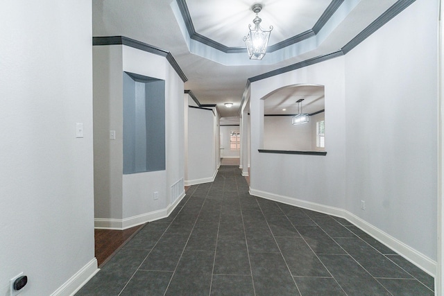 corridor featuring a tray ceiling, an inviting chandelier, dark tile patterned floors, and crown molding