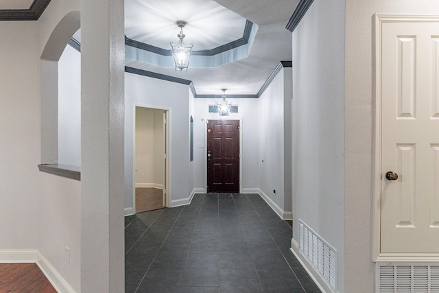 tiled entrance foyer featuring ornamental molding, a tray ceiling, and an inviting chandelier