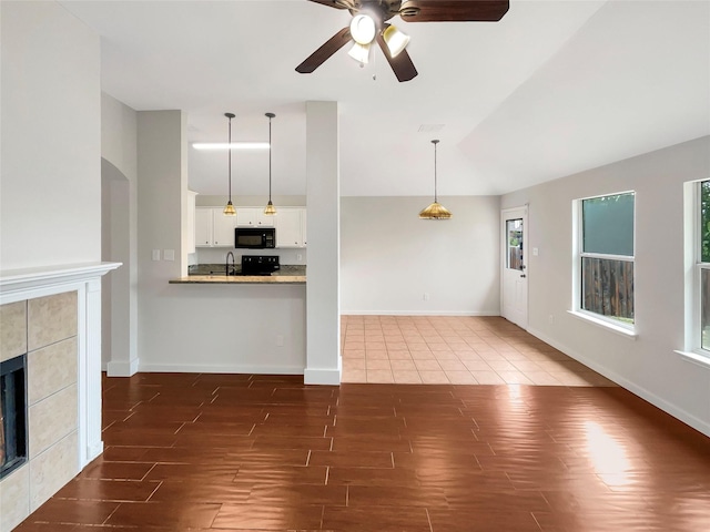 unfurnished living room with ceiling fan, sink, a tiled fireplace, and vaulted ceiling