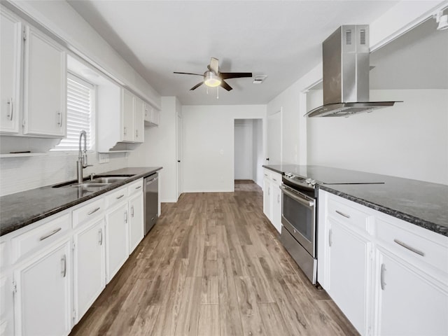 kitchen with white cabinetry, stainless steel appliances, wall chimney range hood, dark stone counters, and light hardwood / wood-style floors