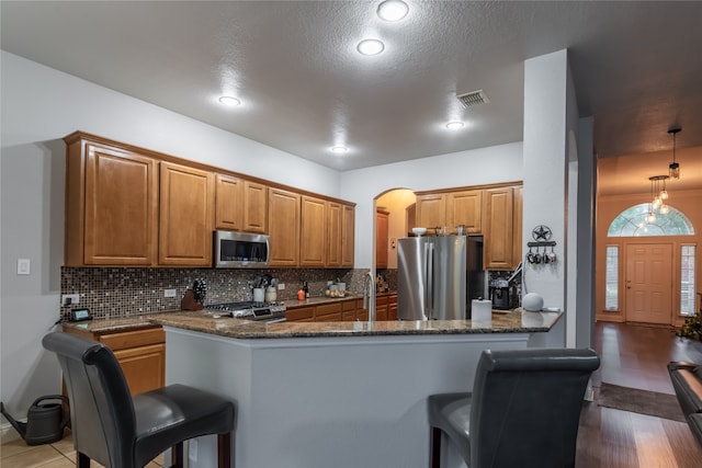 kitchen with dark stone counters, wood-type flooring, tasteful backsplash, stainless steel appliances, and kitchen peninsula