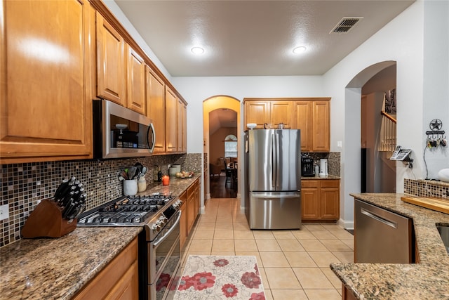 kitchen featuring light tile patterned flooring, appliances with stainless steel finishes, tasteful backsplash, and stone countertops