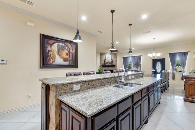 kitchen with an island with sink, sink, light stone counters, and light tile flooring