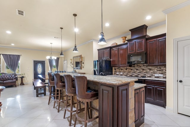 kitchen with decorative light fixtures, tasteful backsplash, black appliances, an island with sink, and light tile floors