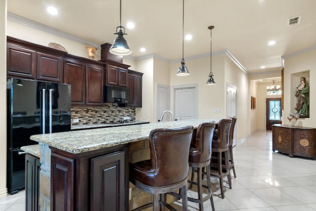 kitchen featuring decorative light fixtures, light tile flooring, backsplash, black appliances, and an island with sink