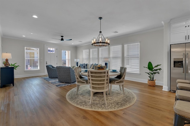 dining space with crown molding, light wood-type flooring, and ceiling fan with notable chandelier