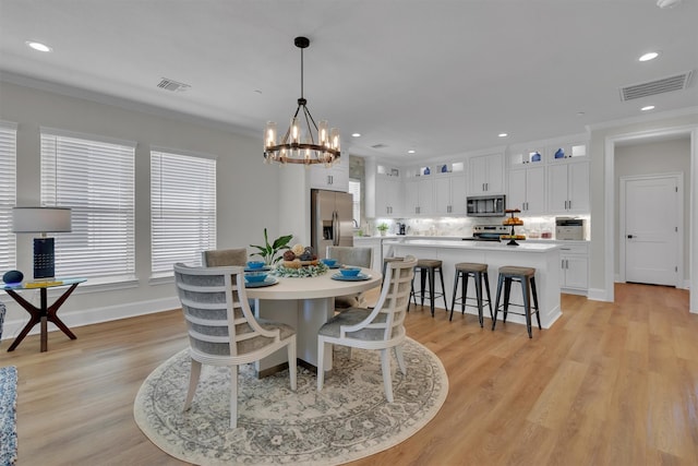 dining room featuring a healthy amount of sunlight, a notable chandelier, light hardwood / wood-style flooring, and crown molding