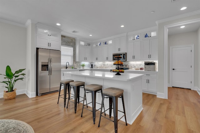 kitchen with a kitchen island, light hardwood / wood-style flooring, stainless steel appliances, white cabinets, and tasteful backsplash