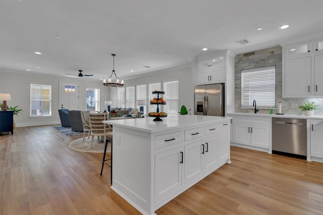 kitchen with light wood-type flooring, a kitchen island, hanging light fixtures, white cabinetry, and appliances with stainless steel finishes