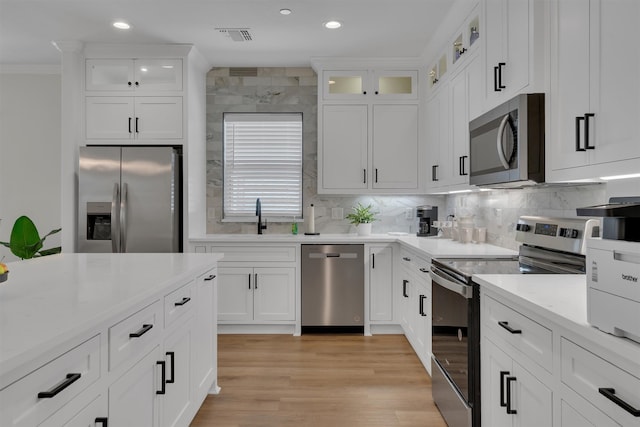 kitchen with light hardwood / wood-style flooring, backsplash, sink, white cabinets, and appliances with stainless steel finishes