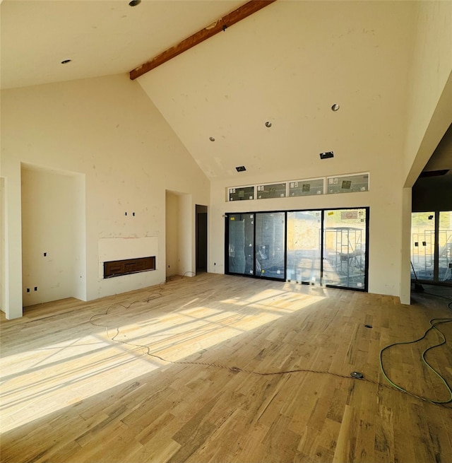 unfurnished living room with beam ceiling, light hardwood / wood-style flooring, and high vaulted ceiling