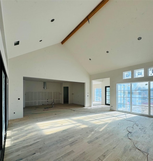 unfurnished living room featuring beam ceiling, light hardwood / wood-style flooring, and high vaulted ceiling