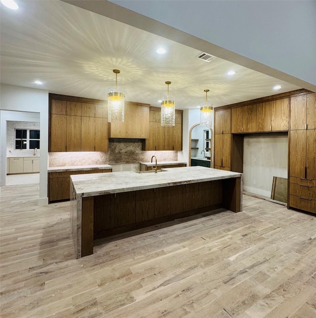 kitchen with a large island with sink, sink, light hardwood / wood-style flooring, and decorative light fixtures