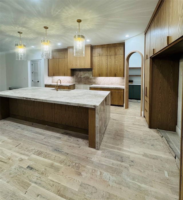 kitchen featuring tasteful backsplash, sink, light hardwood / wood-style floors, and decorative light fixtures