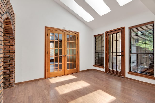 empty room with french doors, a skylight, high vaulted ceiling, and light hardwood / wood-style floors