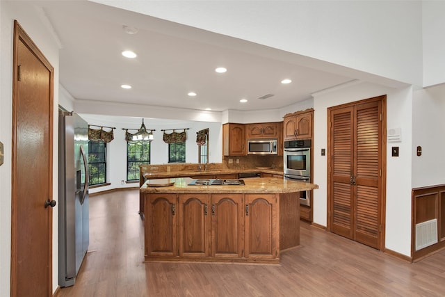 kitchen featuring decorative backsplash, light wood-type flooring, light stone counters, kitchen peninsula, and stainless steel appliances