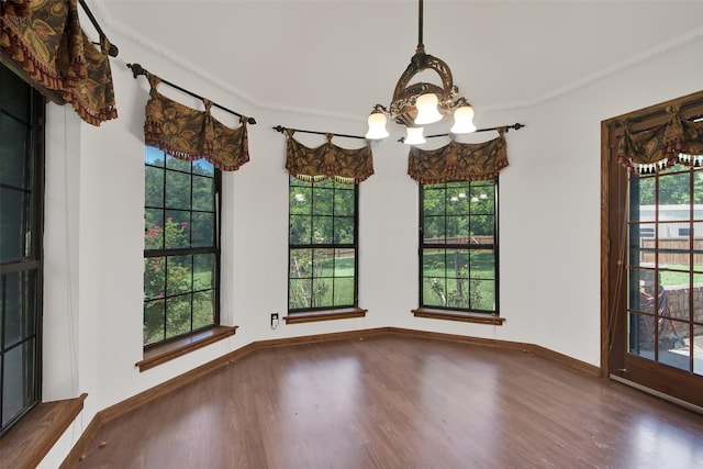 unfurnished dining area featuring plenty of natural light, dark hardwood / wood-style floors, crown molding, and an inviting chandelier