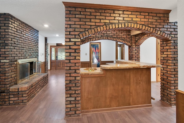 kitchen with kitchen peninsula, hardwood / wood-style floors, a textured ceiling, and a brick fireplace