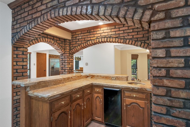 kitchen featuring crown molding, stainless steel refrigerator with ice dispenser, brick wall, kitchen peninsula, and beverage cooler