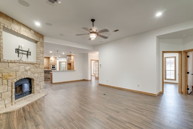 unfurnished living room with hardwood / wood-style flooring, ceiling fan, and a stone fireplace