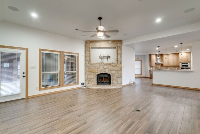 unfurnished living room with light hardwood / wood-style floors, a stone fireplace, and ceiling fan