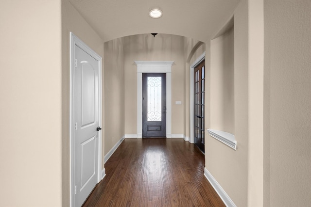 foyer with dark wood-type flooring, arched walkways, and baseboards