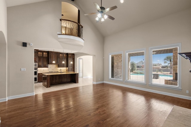 unfurnished living room featuring baseboards, arched walkways, ceiling fan, and light wood finished floors