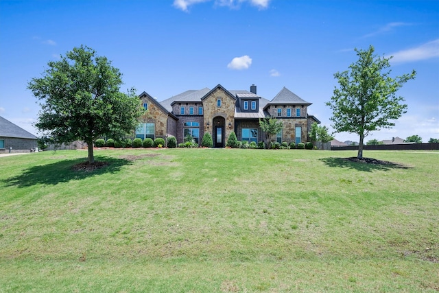 french country style house featuring a standing seam roof, a front yard, and stone siding