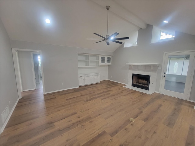 unfurnished living room featuring beam ceiling, a tiled fireplace, visible vents, wood finished floors, and ceiling fan