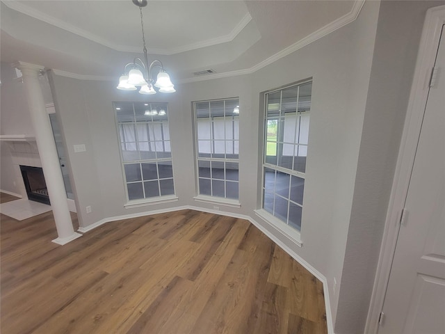 unfurnished dining area with wood finished floors, a fireplace with flush hearth, a raised ceiling, a notable chandelier, and visible vents
