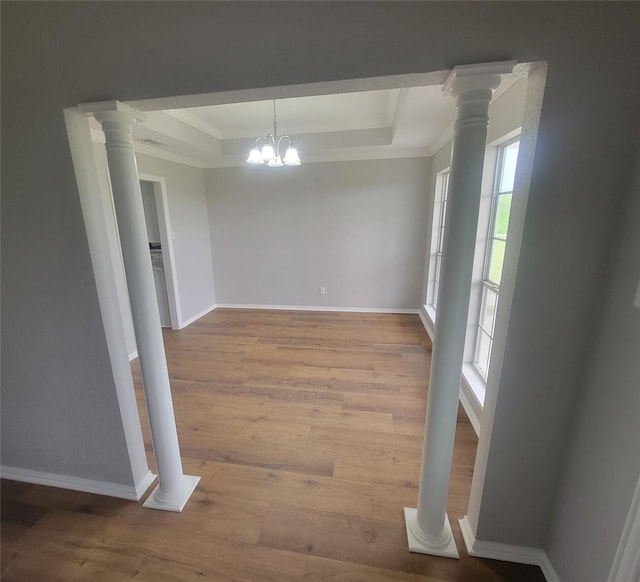 unfurnished dining area featuring baseboards, wood finished floors, a raised ceiling, and ornamental molding