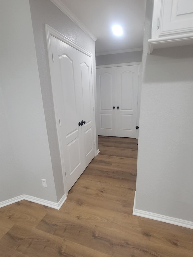 corridor with wood finished floors, baseboards, and ornamental molding