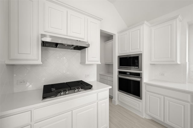 kitchen with decorative backsplash, white cabinets, stainless steel appliances, and vaulted ceiling