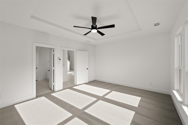 unfurnished bedroom featuring a tray ceiling, ensuite bath, ceiling fan, and light colored carpet