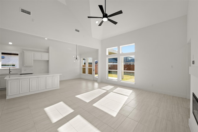 unfurnished living room featuring sink, ceiling fan with notable chandelier, high vaulted ceiling, and light tile patterned flooring