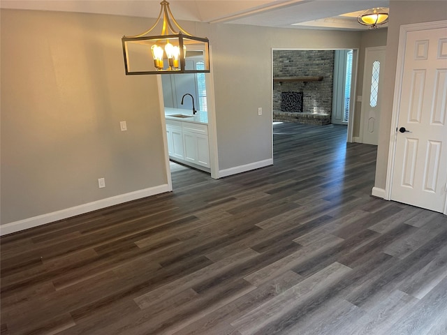 unfurnished dining area with a fireplace, sink, dark wood-type flooring, and a chandelier