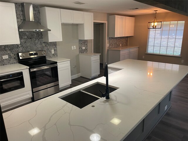 kitchen featuring light stone counters, wall chimney exhaust hood, electric stove, an inviting chandelier, and hanging light fixtures