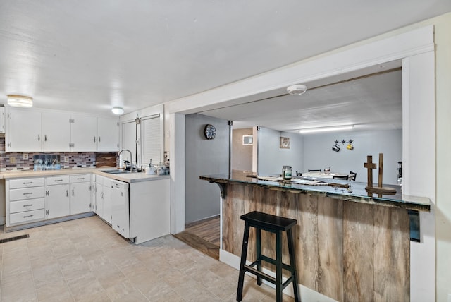 kitchen featuring kitchen peninsula, backsplash, white dishwasher, sink, and white cabinets