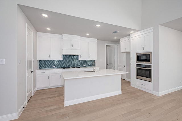 kitchen featuring appliances with stainless steel finishes, a kitchen island with sink, sink, light hardwood / wood-style floors, and white cabinetry