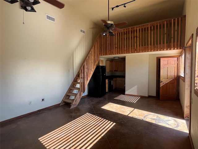 unfurnished living room featuring dark tile flooring, a high ceiling, ceiling fan, and rail lighting