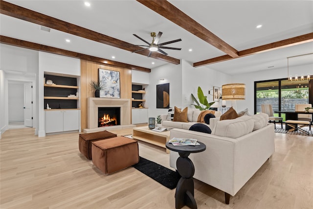 living room featuring ceiling fan, built in shelves, light hardwood / wood-style flooring, and beamed ceiling