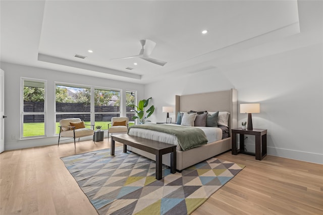 bedroom featuring ceiling fan, a raised ceiling, and light hardwood / wood-style flooring