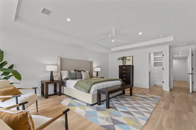 bedroom with a raised ceiling, ceiling fan, and light wood-type flooring