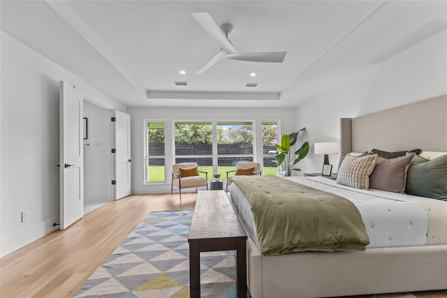 bedroom featuring ceiling fan, a raised ceiling, and light wood-type flooring