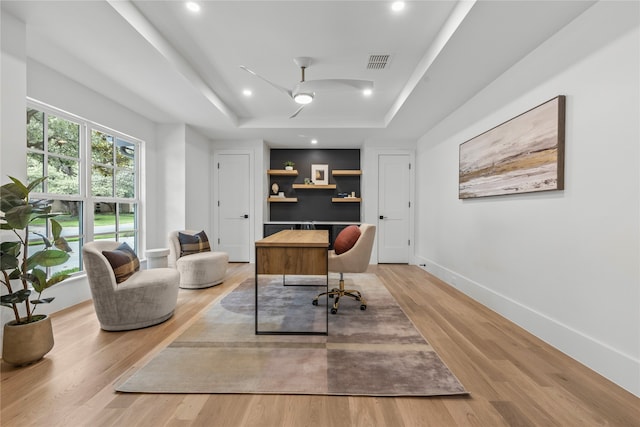 home office with ceiling fan, a raised ceiling, and light hardwood / wood-style floors